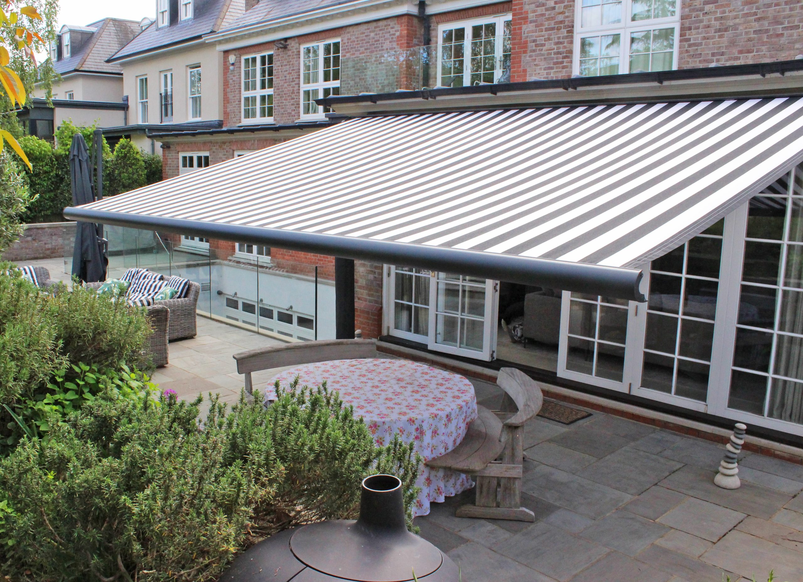 Anthracite grey cassette awning with integrated lighting extended over a terrace at dusk, outdoor sofa and fire bowl beneath