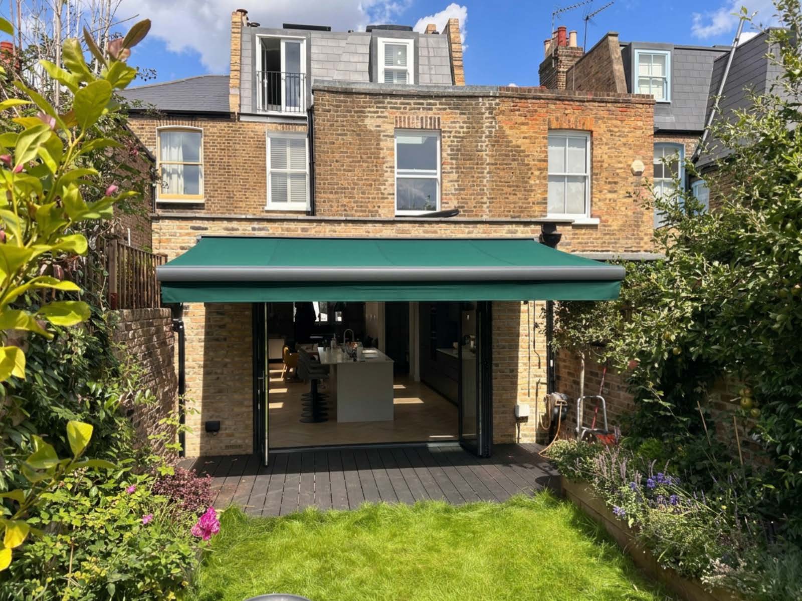 Simple full cassette awning in terracotta fabric fitted above a back door in a small walled courtyard garden