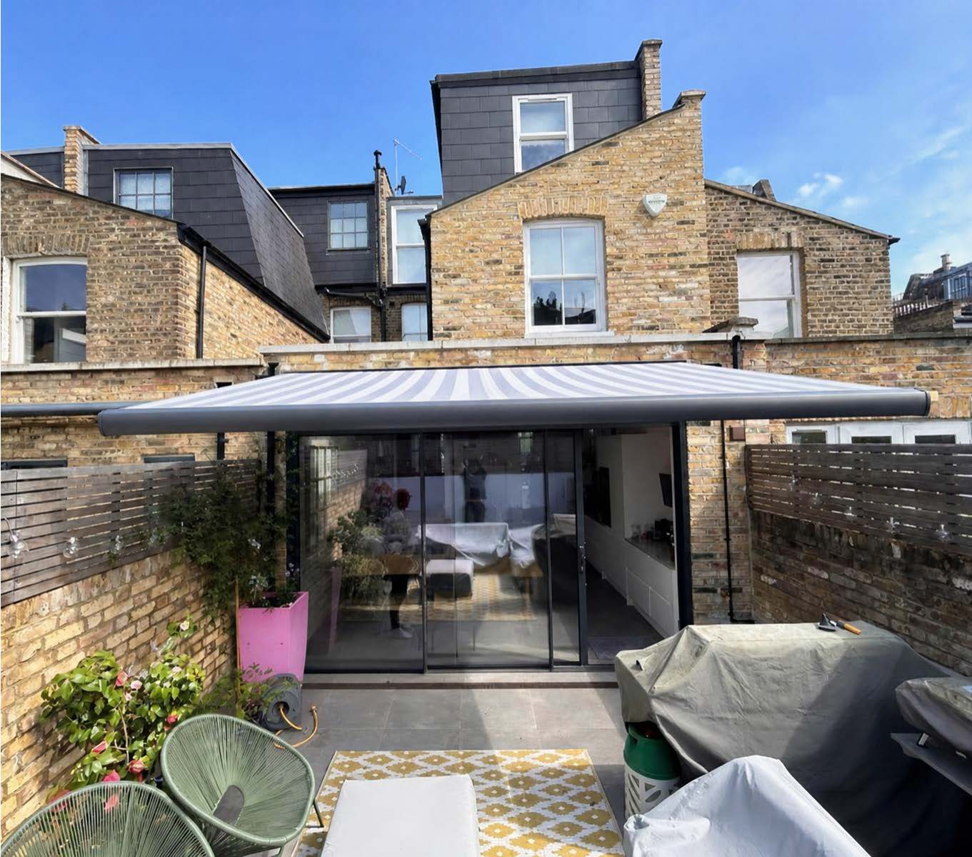 Compact cassette awning with a protective hood fitted above French doors on a London brick house, bistro table on the patio below