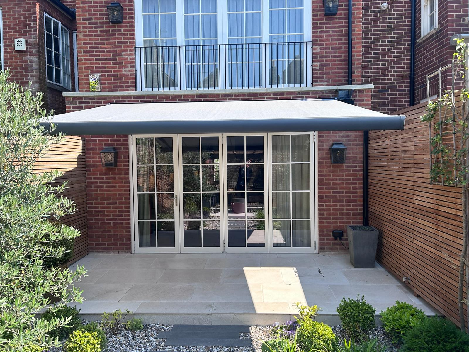 Wide sand coloured awning fitted above bifold doors on a London townhouse, shading a garden dining table